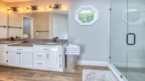 A modern bathroom with a large vanity, a shower with a glass door, and a hexagonal window.