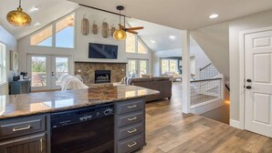 A spacious kitchen with a large island, a fireplace, and a dining area with a high ceiling and large windows.