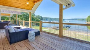 A covered deck with a wooden floor, a sofa with cushions, and a view of a lake with boats.