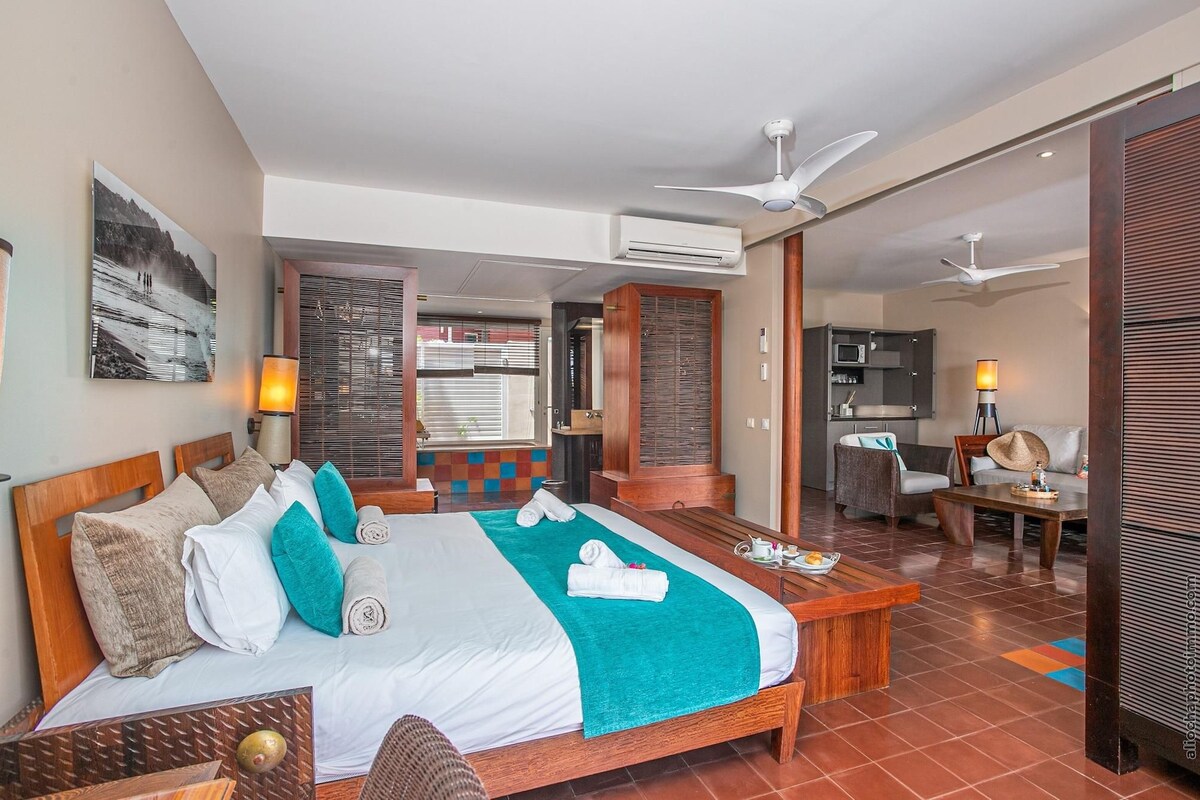 Quarto de hotel com cama, escrivaninha, cadeira e televisão.