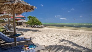 A beach with lounge chairs, a thatched umbrella, and a view of the ocean. - Les Villas du Lagon (Le Francois)