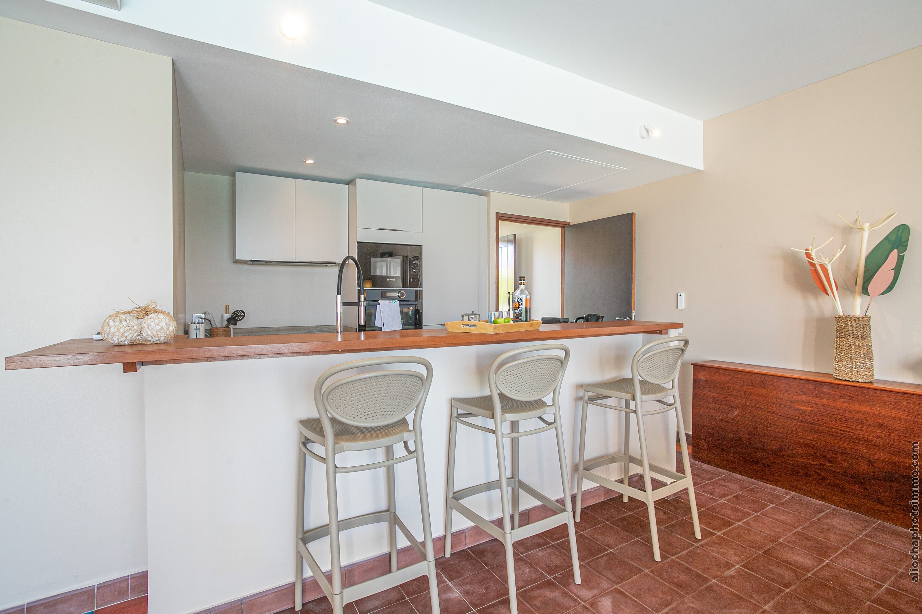 A modern kitchen with a bar area, including a countertop, bar stools, and a refrigerator.