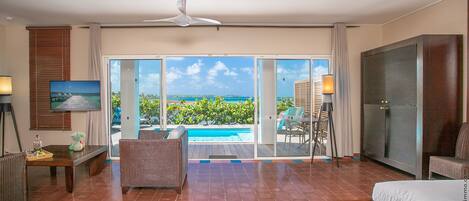 A hotel room with a bed, a dining table, a TV, and a view of the ocean.