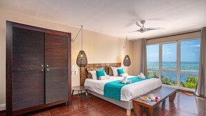 A hotel room with a bed, a dining table, a view of the ocean, a ceiling fan, and a wardrobe. - Les Villas du Lagon (Le Francois)