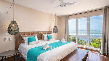 A hotel room with a large bed, a view of the sea, a ceiling fan, and a table with breakfast items.