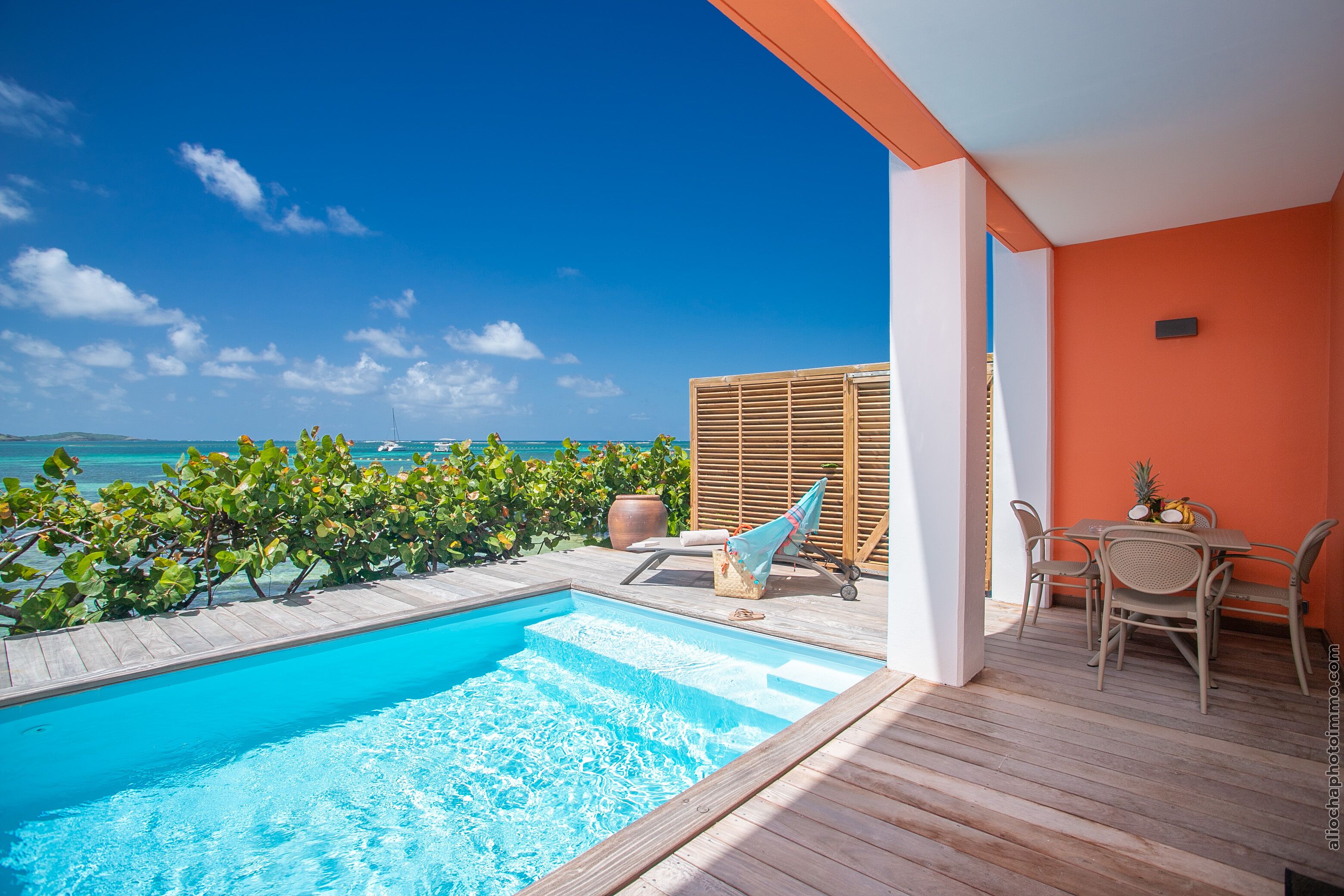 A pool area with a view of the ocean, wooden deck, and a table with chairs.