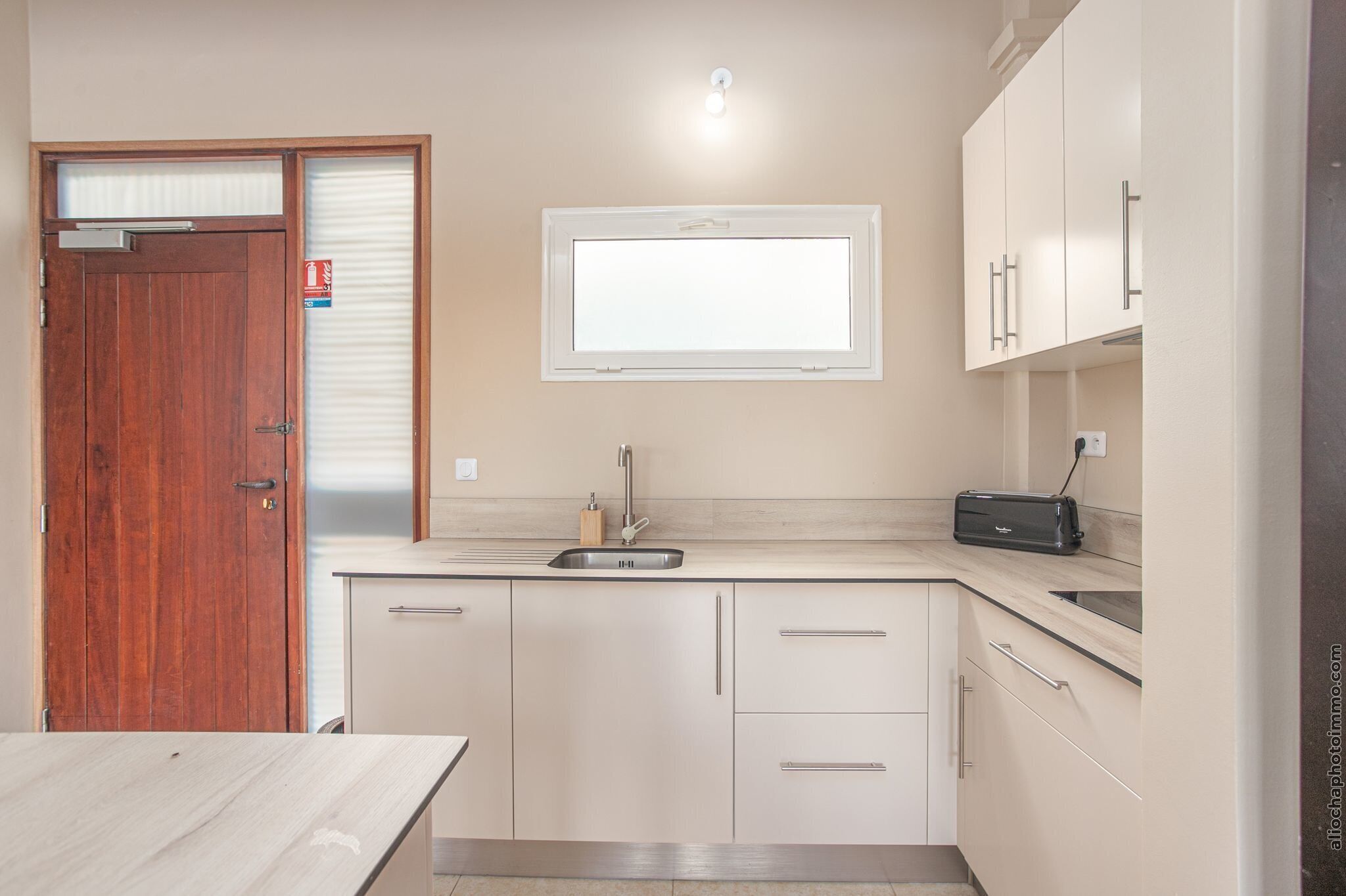A compact kitchen with a wooden door, a window above the sink, and a toaster on the countertop.