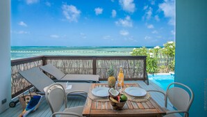 A wooden deck with a table set for two, overlooking a clear blue ocean and a swimming pool. - Les Villas du Lagon (Le Francois)