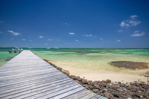 A wooden pier leading to a beach with clear turquoise water and a distant boat. - Les Villas du Lagon (Le Francois)