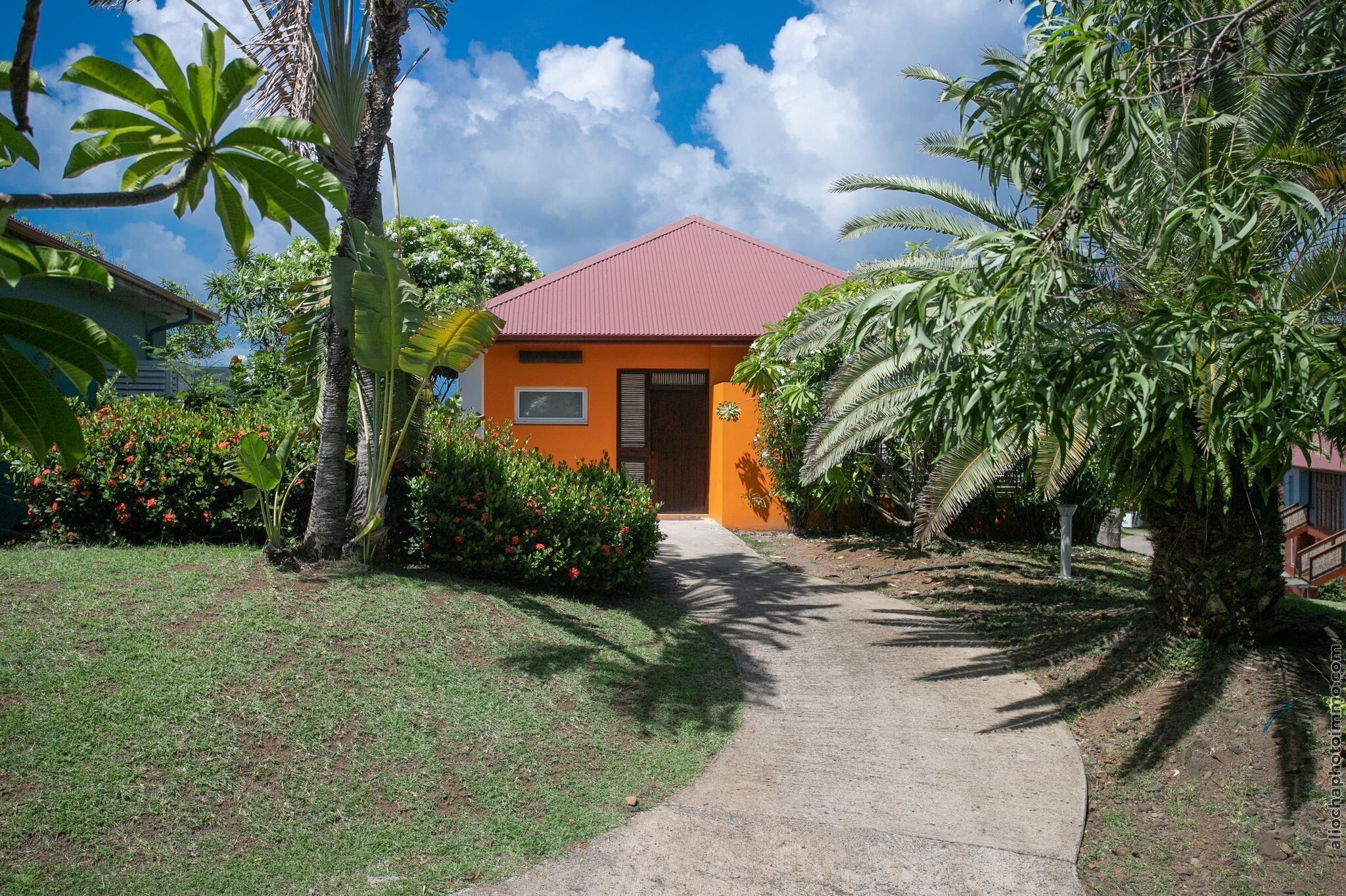 A house with a red roof, surrounded by lush greenery and a clear sky.