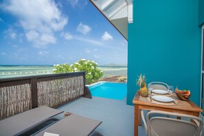 A wooden deck with a table set for two, overlooking a clear blue pool and ocean view. - Les Villas du Lagon (Le Francois)