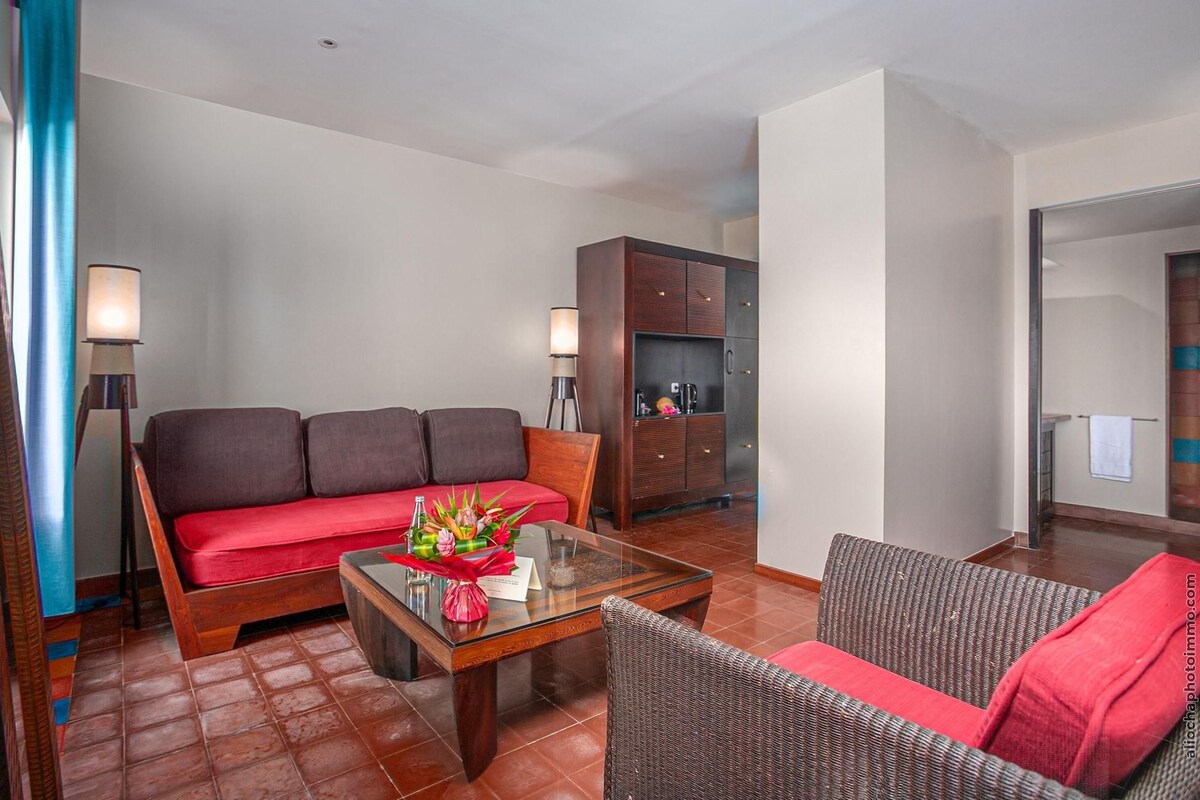 Sala de estar com sofá, mesa de centro com arranjo floral, armário e cadeira de vime.