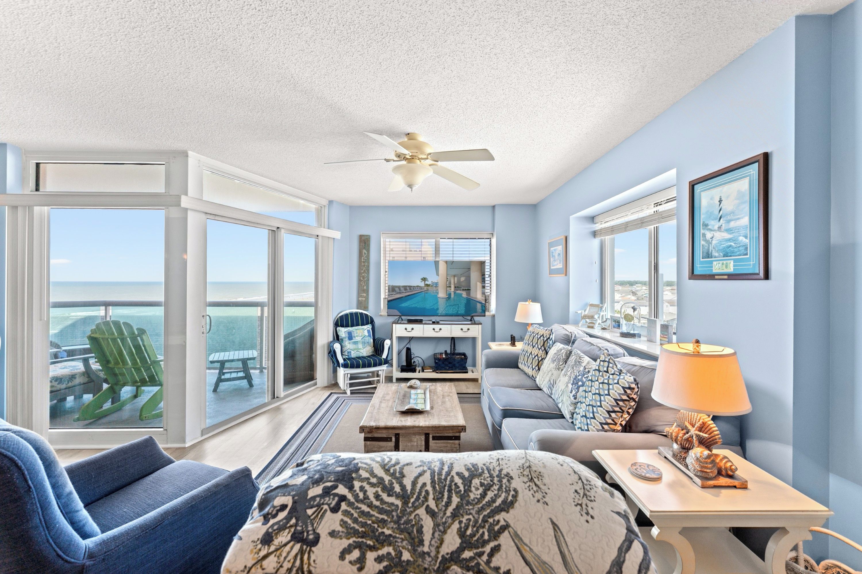 A spacious living room with a view of the ocean, a ceiling fan, and a dining area with a view of the pool.