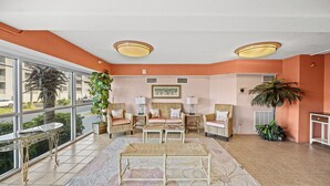 A spacious living room with a large window, two sofas, a coffee table, and a potted plant. - Laguna Keyes 612 - Corner Condo - 1 Bedroom - Ocean Front (North Myrtle Beach)