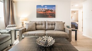 Ein Wohnzimmer mit einer Couch, einem Couchtisch mit einer dekorativen Metallschale, einer Lampe und einem Gemälde einer Berglandschaft.