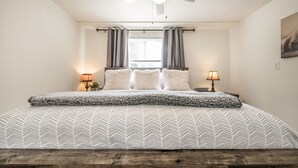Ein Schlafzimmer mit einem Bett, zwei Nachttischlampen, einem Deckenventilator und einem Fenster mit Vorhängen.