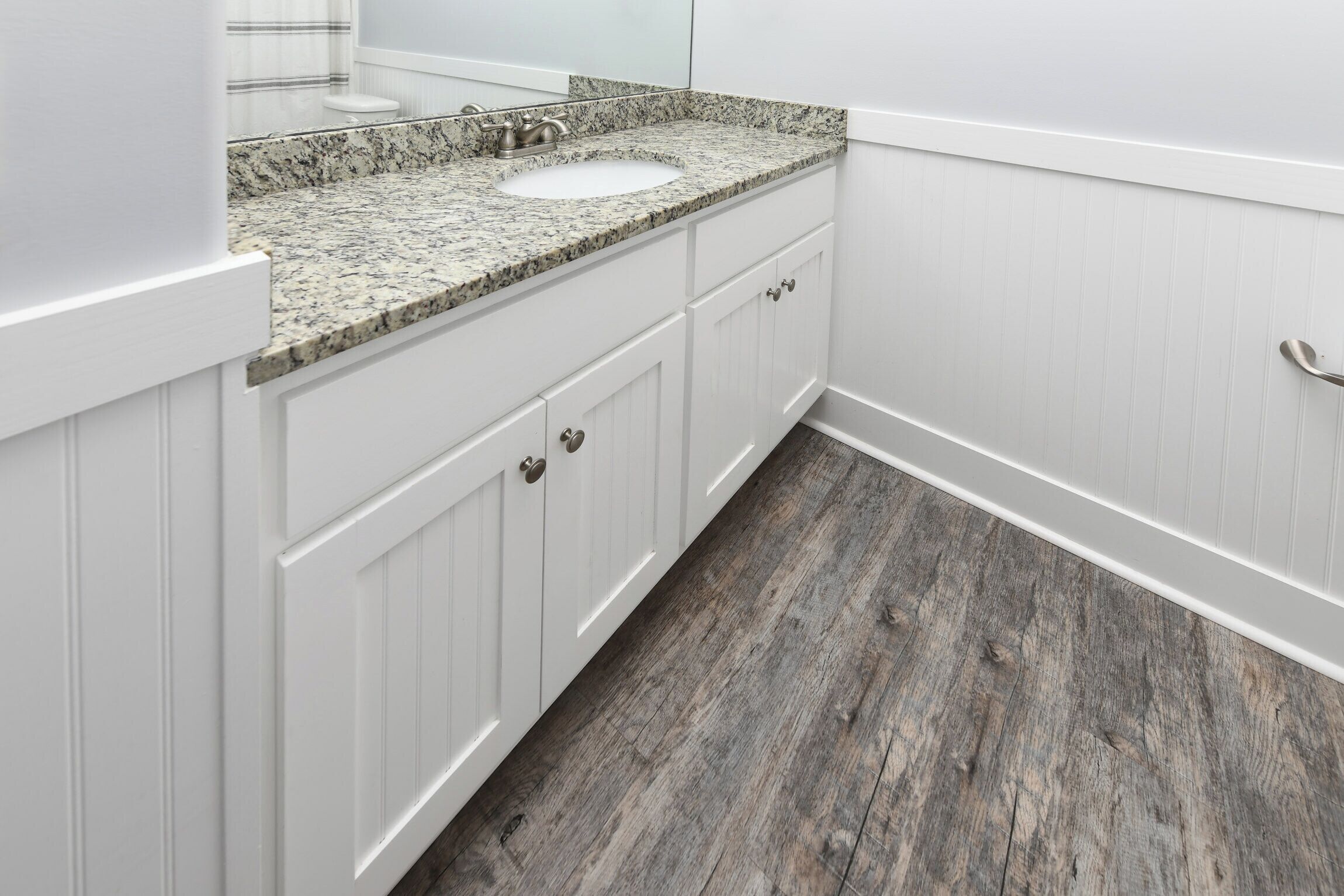 Un baño con muebles blancos, encimera de granito y suelo de madera.