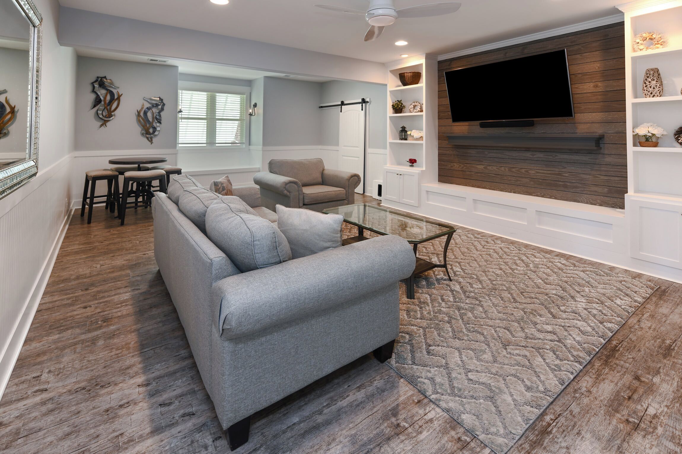 Una sala de estar moderna con un sofá modular gris, una mesa de centro de vidrio y piso de madera.