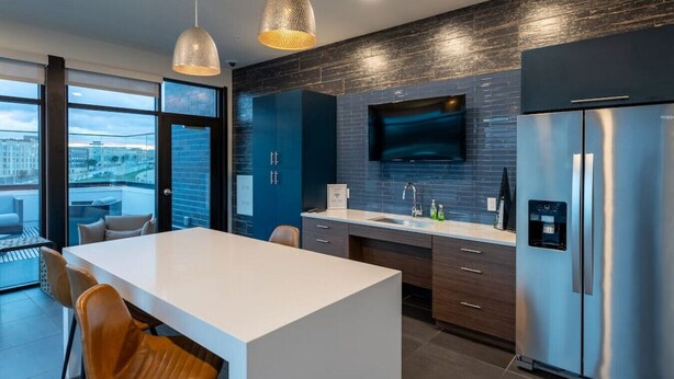 A modern kitchen with a large island, dark cabinetry, stainless steel appliances, and a city view through large windows. - Modern Luxury 1BR Apt with Rooftop, Gym, and Parking (Milwaukee)