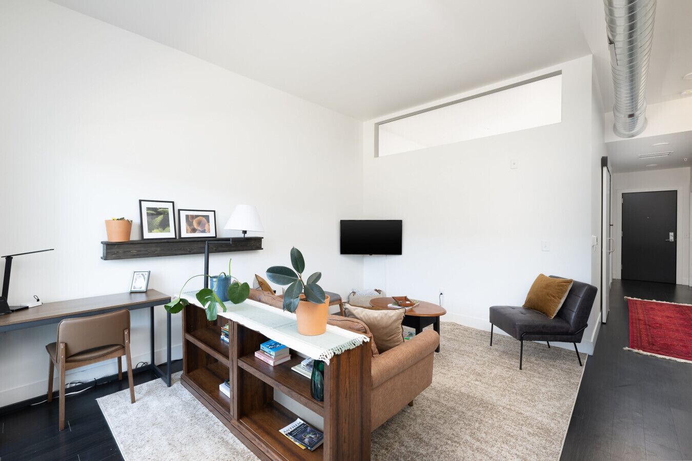 Ett modernt vardagsrum med en soffa, ett soffbord, ett skrivbord och en tv som är monterad på väggen.