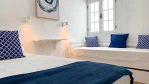 Ein Zimmer mit zwei Betten, einem Gemälde, einem Fenster und einer Wandleuchte.