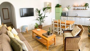 Ein modernes Wohnzimmer mit Sofa, Couchtisch und Esstisch. Es gibt eine Küchenzeile mit Mikrowelle und Regalen.