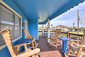 Eine überdachte Veranda mit Holzmöbeln, darunter Stühle und Tische, mit Blick auf ein Wohngebiet mit Häusern und Palmen.
