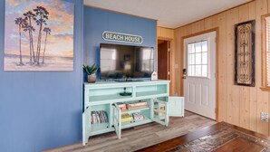 Una habitación con pared azul, un letrero que dice 'BEACH HOUSE', un televisor y una puerta de madera.