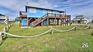 Un edificio de dos pisos con fachada azul, una terraza de madera y una escalera que lleva al nivel superior.