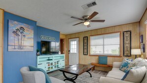 Una sala de estar con televisor, ventilador de techo, mesa de centro y sofá.