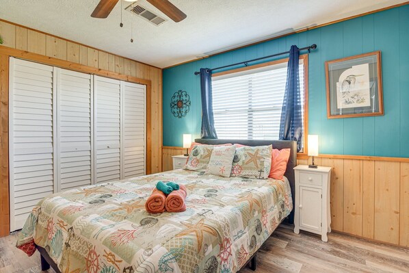 A bedroom with a bed, a nightstand, a window with curtains, a wall clock, and a framed picture.