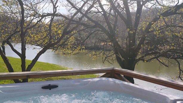 A hot tub with a wooden deck and a view of a lake and trees.