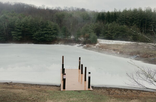Une jetée en bois s’étendant sur un lac gelé, entouré d’une forêt dense.