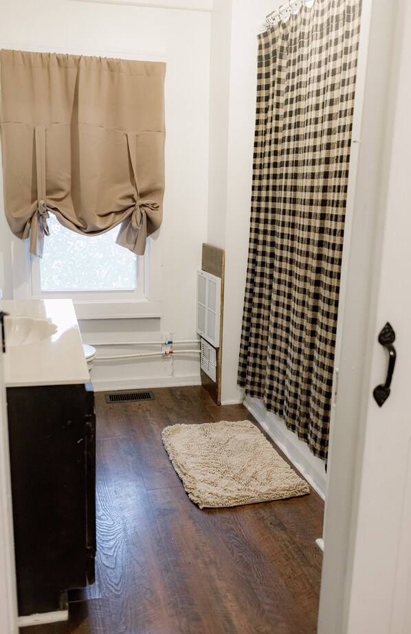 Une salle de bain avec une fenêtre, un lavabo, des toilettes, un rideau de douche et un tapis.