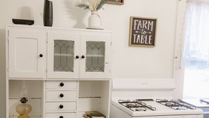 A kitchen with a white stove, a white cabinet with glass doors, and wall decor including signs with farm-related phrases.