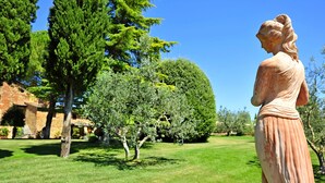 Una estatua en un parque con árboles y una estructura de ladrillo al fondo.