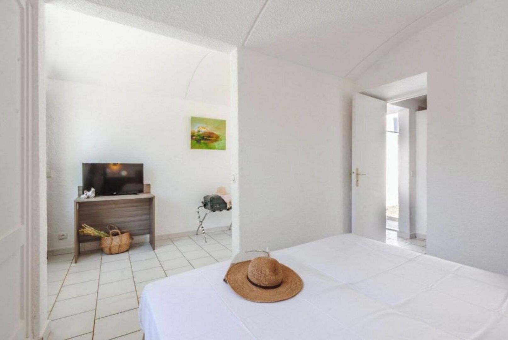Une chambre d’hôtel avec un lit, un téléviseur posé sur un meuble en bois, un tableau accroché au mur et une valise sur le sol.