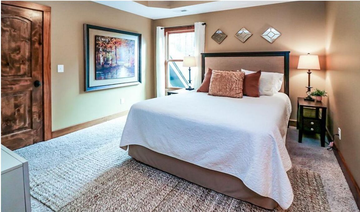 A hotel room with a large bed, a nightstand with a lamp, a painting on the wall, and a window with curtains.
