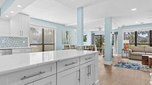 A modern kitchen with white cabinets, a marble countertop, and a dining area with a table and chairs. - "Pipers Perch" - Book Fall Break with Golf Cart! (Miramar Beach)