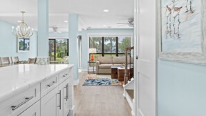A modern kitchen with white cabinetry, a large island, and a chandelier. There is a dining area with a table and chairs, and a living room with a sofa and a coffee table. - "Pipers Perch" - Book Fall Break with Golf Cart! (Miramar Beach)