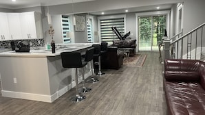 A modern kitchen with a central island, bar stools, a dining area with a piano, and a living room with a leather couch. - Modern newly private basement apartment  (Alexandria)