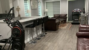 A modern kitchen with a bar area, a treadmill, and a living room with a brown leather sofa. - Modern newly private basement apartment  (Alexandria)