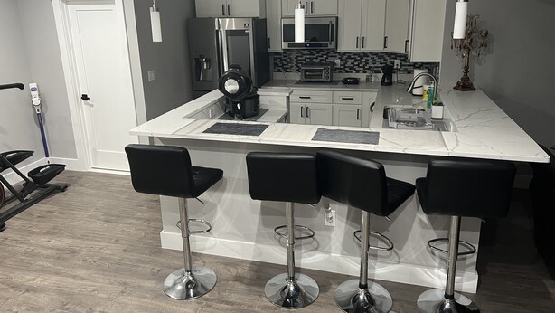 A modern kitchen with white cabinets, a central island with bar stools, a built-in microwave, and a coffee maker. - Modern newly private basement apartment  (Alexandria)