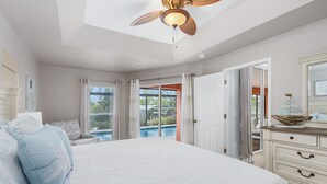 A bedroom with a large bed, a ceiling fan, a view of a swimming pool, and a door leading to an outdoor area. - The perfect family vacation home with gulf access/heated pool/tiki bar/ kayaks! (Cape Coral)