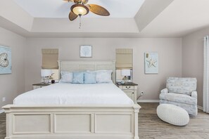 Une chambre à coucher avec un grand lit, deux tables de chevet, une chaise et un ventilateur de plafond.