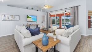 A modern living room with a sofa, a coffee table with a vase, and a TV on the wall. - The perfect family vacation home with gulf access/heated pool/tiki bar/ kayaks! (Cape Coral)