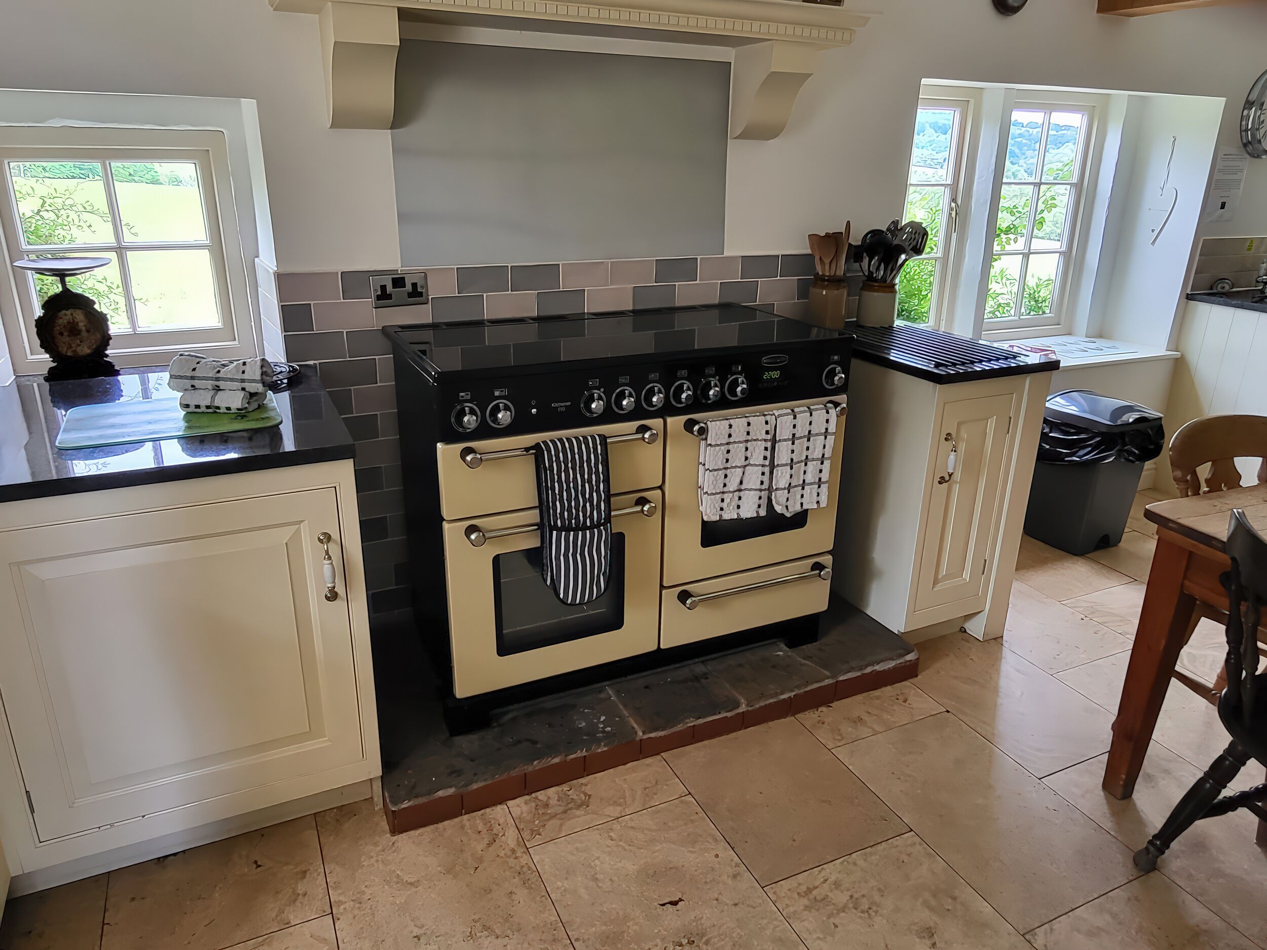 A kitchen with a double oven, a window, and a trash bin.