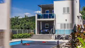 A pool table with paddles, a tennis racket, and a table tennis paddle on a sunny day.