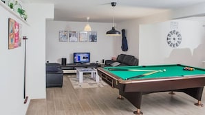 A modern living room with a pool table, a sofa, a television, and a guitar.