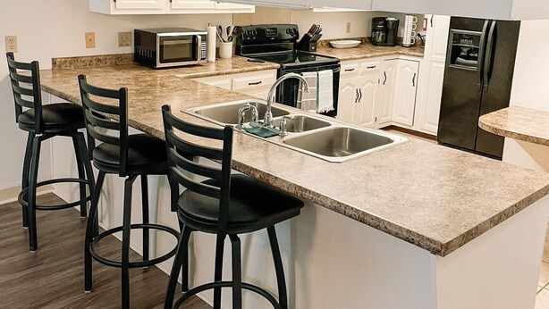 A modern kitchen with white cabinets, a granite countertop, a double sink, a stove, a microwave, and three black bar stools. - 2 BR / 2 BA UNIT! WALKING DISTANCE FROM SQUARE AND CAMPUS!! (Oxford)